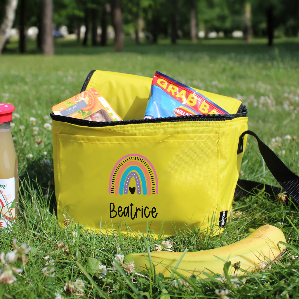 Yellow bag with a rainbow design and 'Beatrice' text, filled with snacks, on grass.