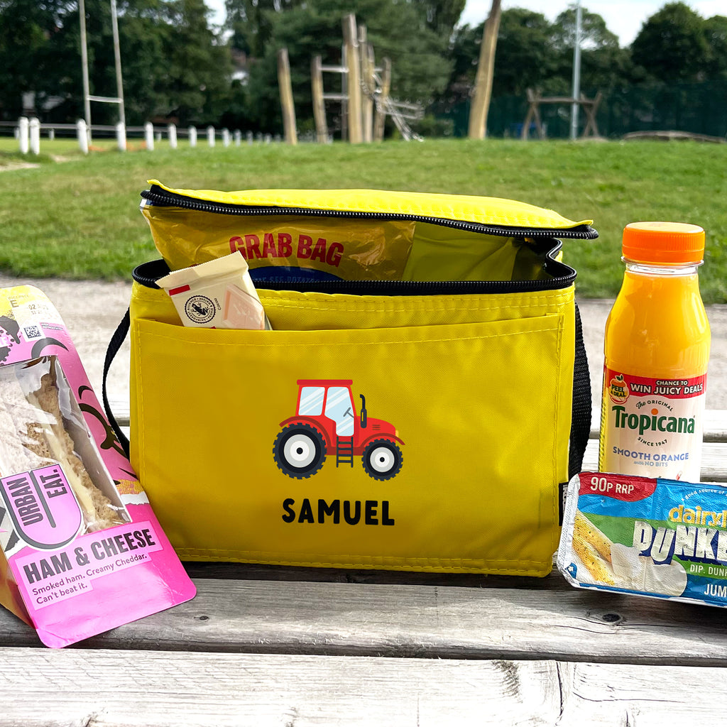 Yellow cooler bag with a tractor design and snacks on a wooden surface outdoors.