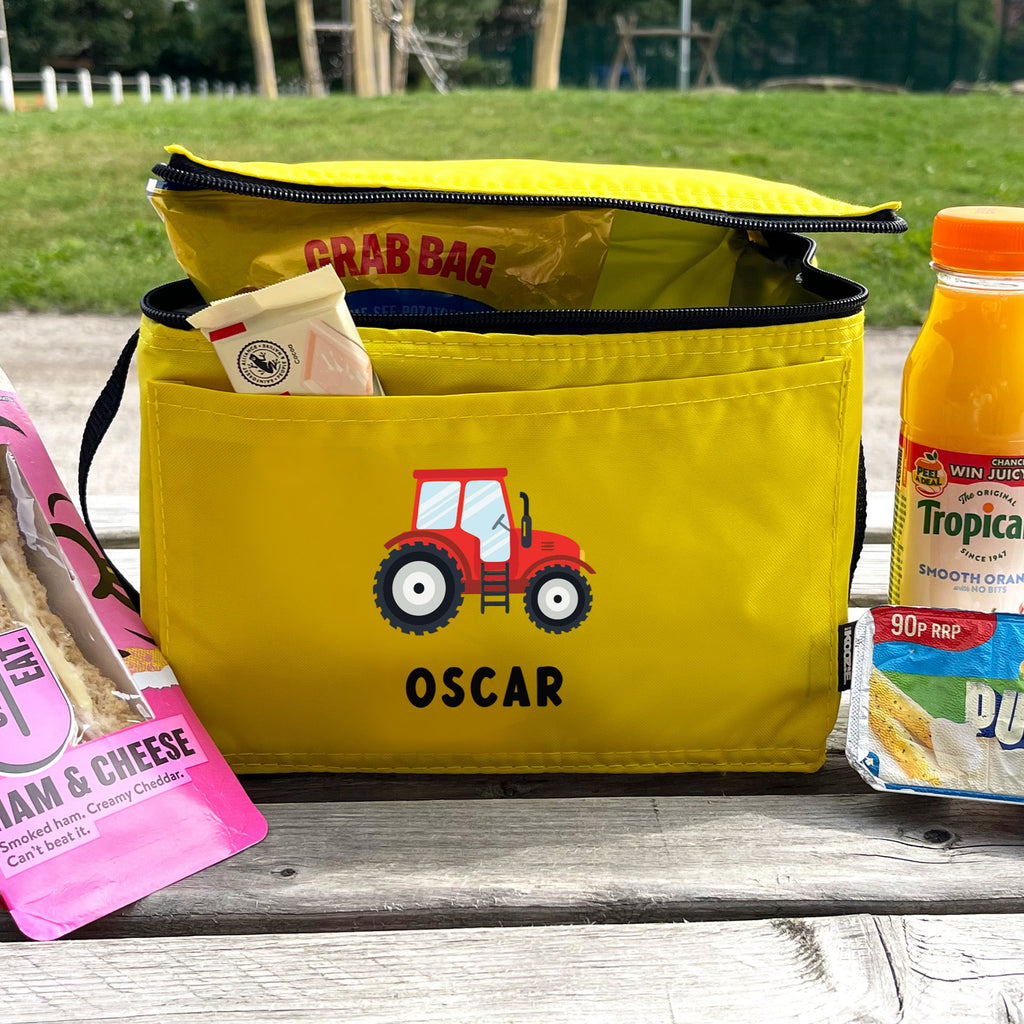 Yellow lunch bag with a tractor design and 'Oscar' branding, containing snacks and drinks on a wooden surface.