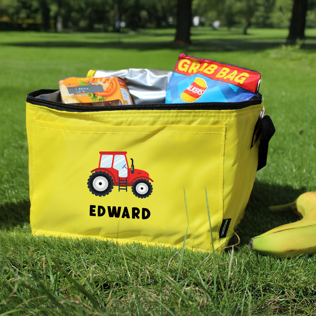 Yellow cooler bag with a red tractor design and 'EDWARD' text, filled with snacks, on grass.