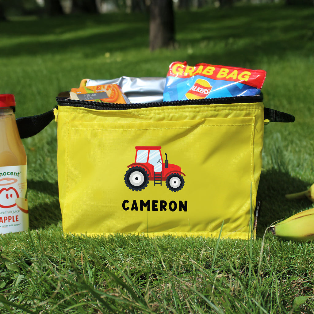 Yellow bag with a red tractor design and 'Cameron' text on grass, with a drink and snacks nearby.