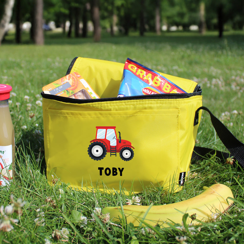 Yellow bag with a red tractor design and 'Toby' text, filled with snacks, on grass.