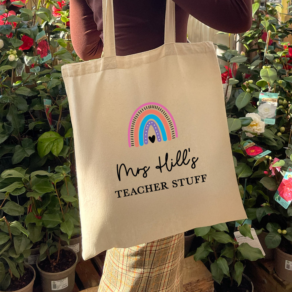 Tote bag with rainbow design and text held by a person in a garden setting