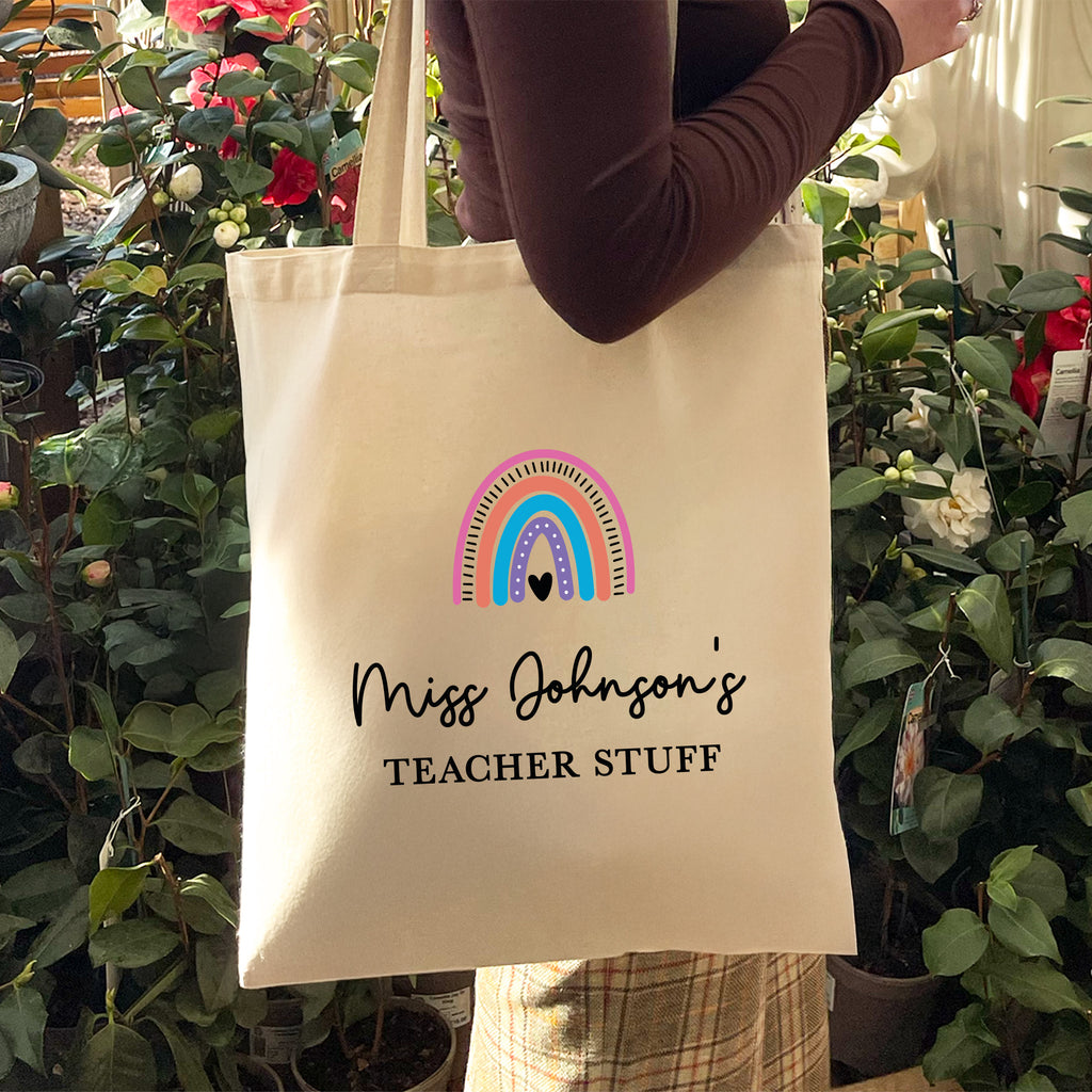 Tote bag with rainbow design and text held by a person in a garden setting