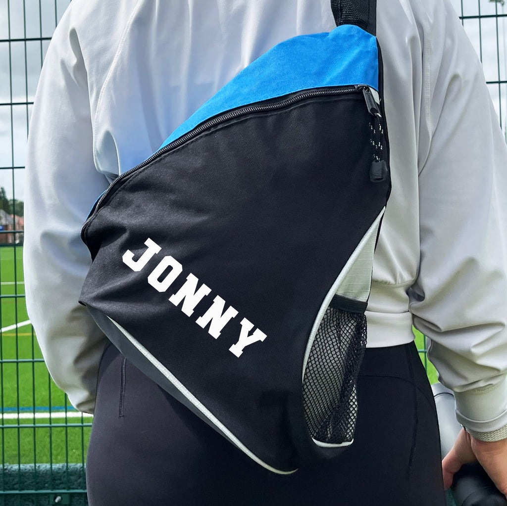 Person wearing a black and blue backpack with 'JONNY' printed on it, standing on a grassy field.