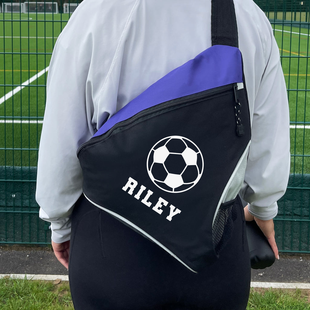Person wearing a black and purple bag with a soccer ball design and 'RILEY' text on a sports field.