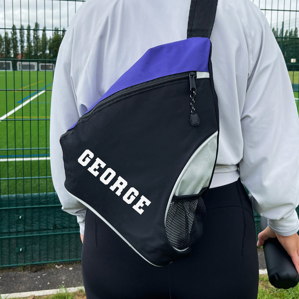 Person wearing a black and purple backpack with 'GEORGE' on it, standing on a sports field.