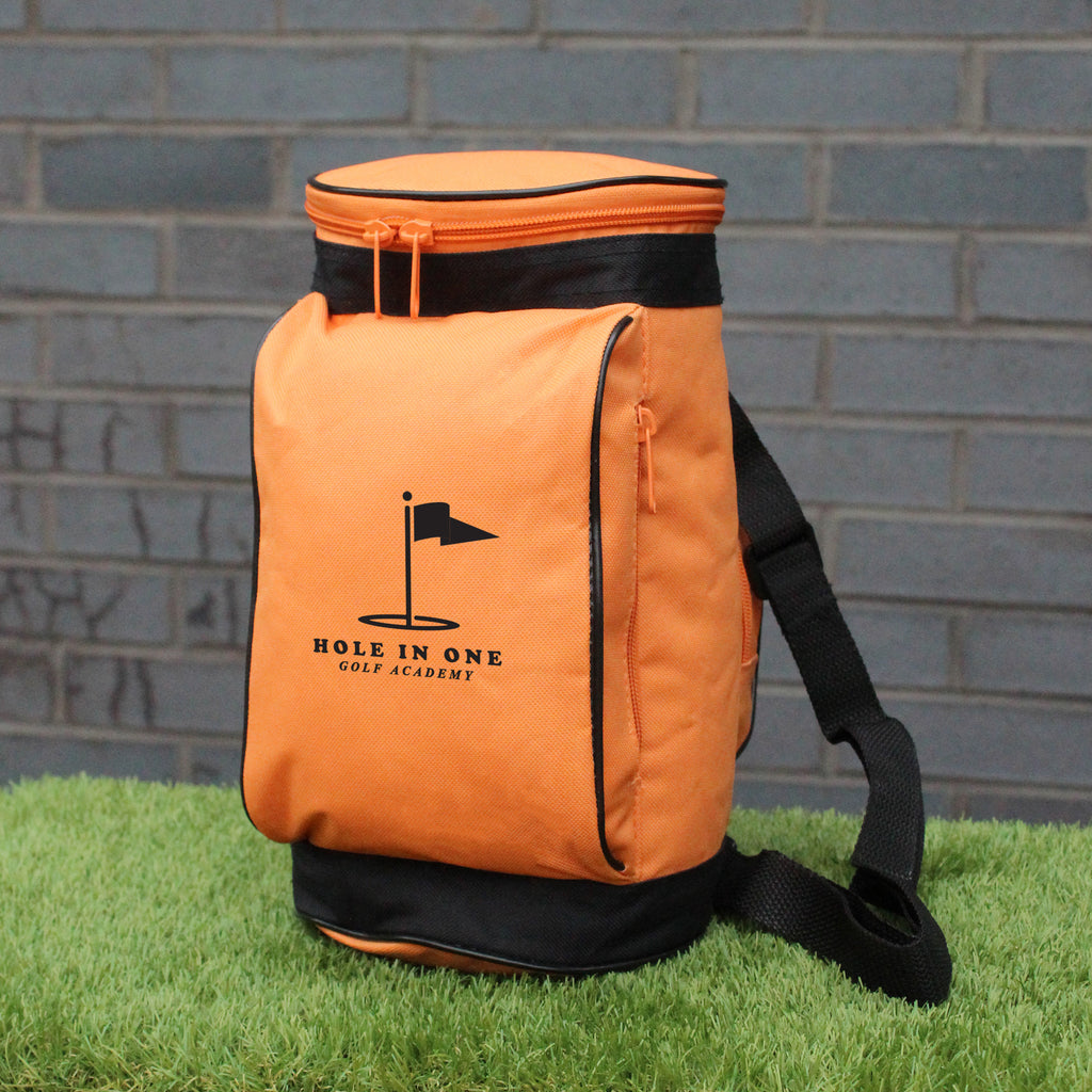 Orange bag with black straps on grass against a brick wall