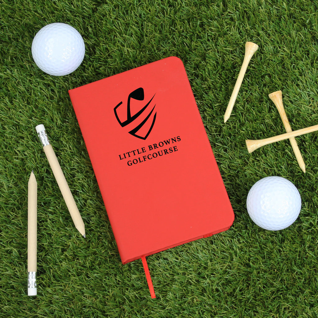 Red notebook with 'Little Browns Golfcourse' logo on grass with golf accessories