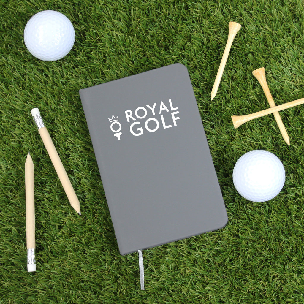 Gray notebook with 'Royal Golf' logo on grass with golf balls and tees
