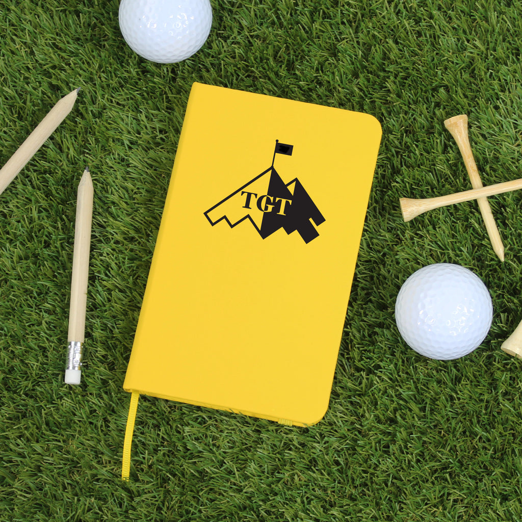 Yellow notebook with a golf-themed design on grass with golf balls and tees.