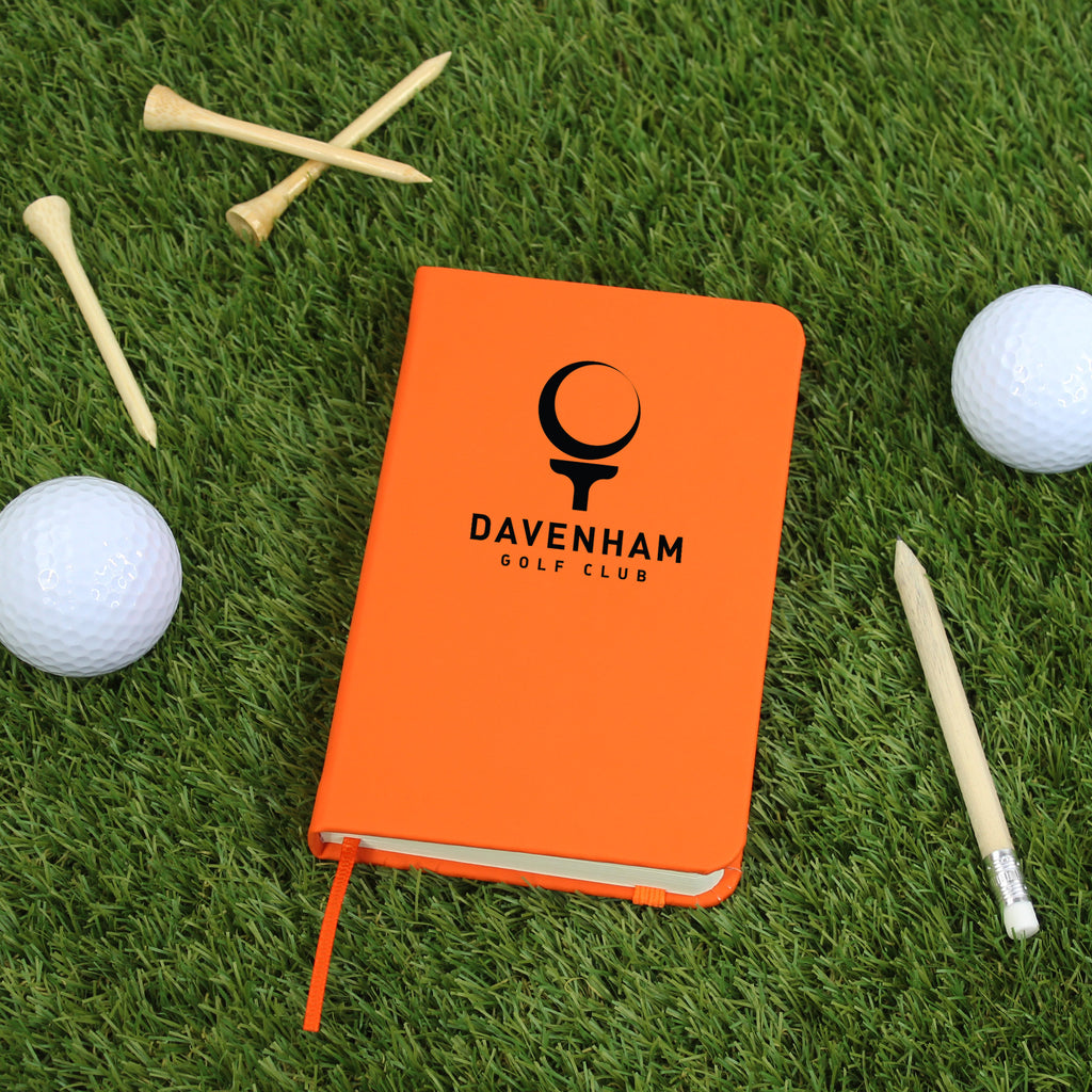 Orange notebook with Davenham Golf Club logo on grass with golf balls and tees