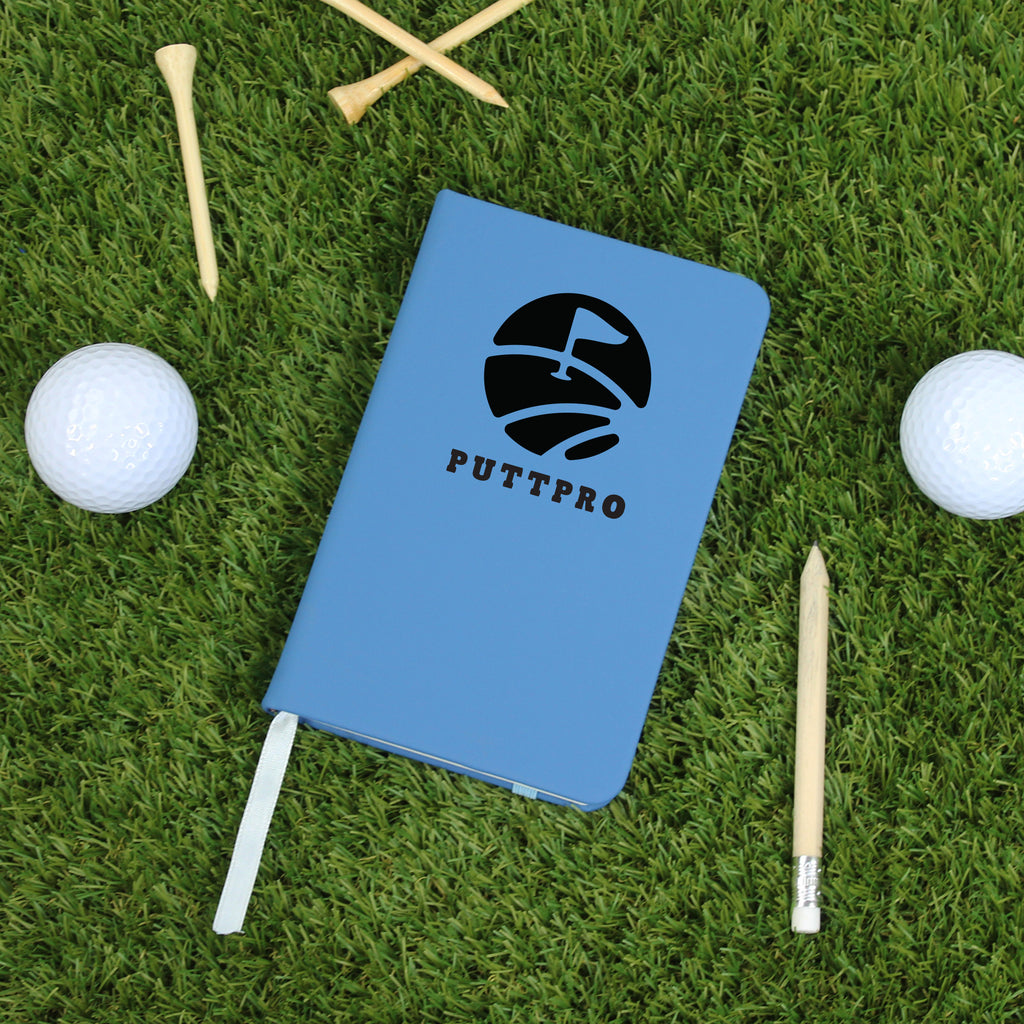 Blue notebook with 'PUTTPRO' logo on grass with golf balls and tees