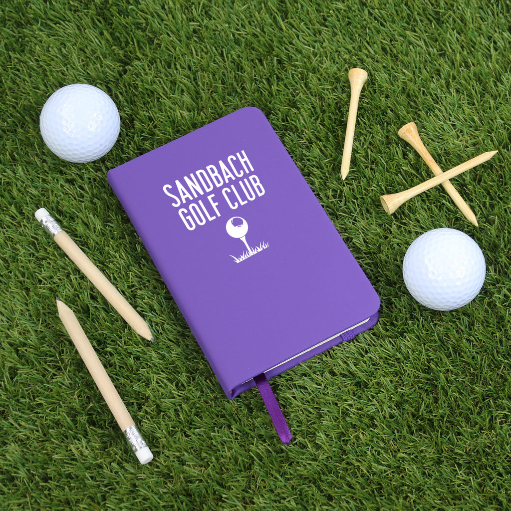 Purple notebook with 'Sandbach Golf Club' text on grass with golf accessories