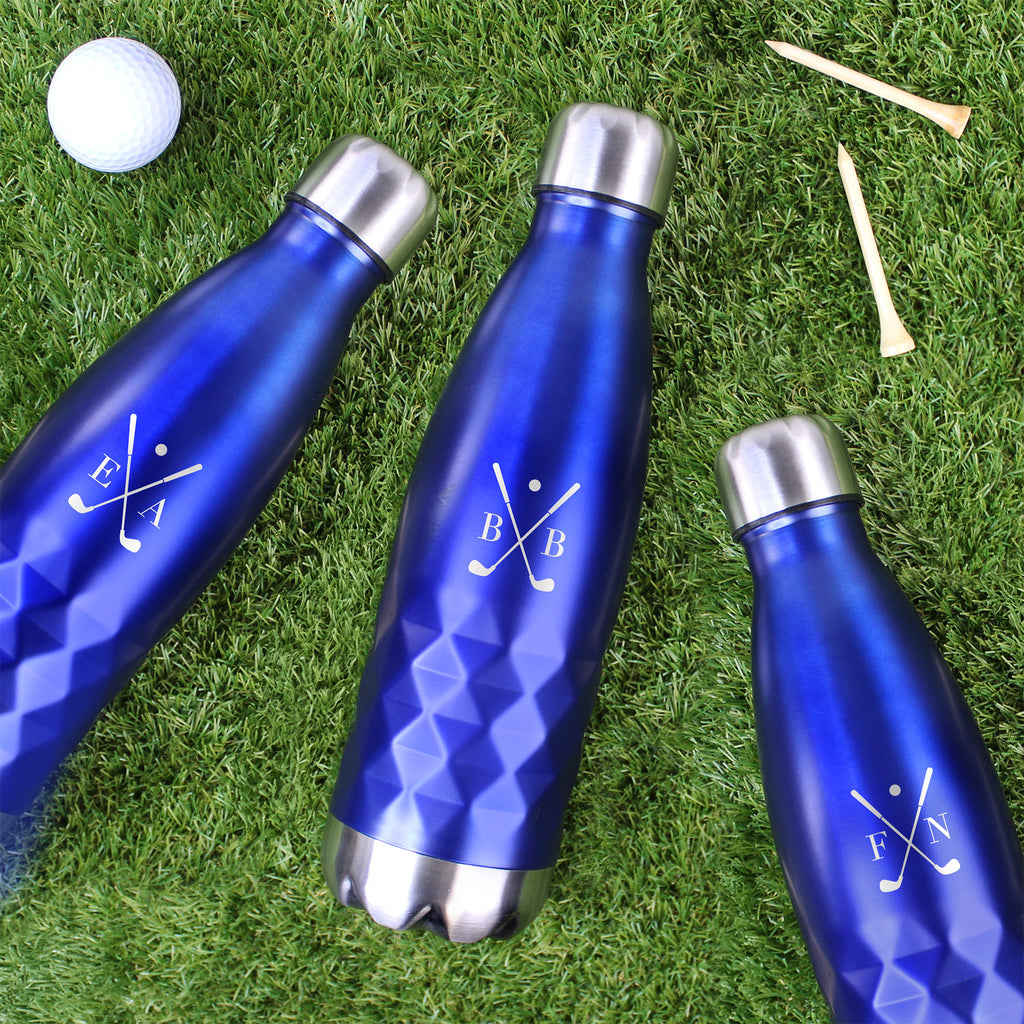 Three blue water bottles with silver caps on grass next to a golf ball and tees.