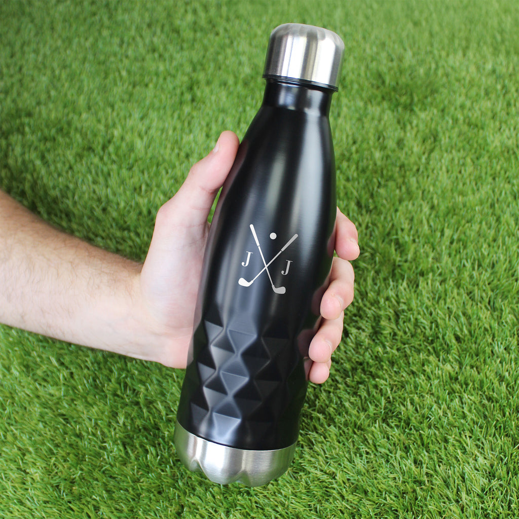 Black water bottle with silver cap held by a hand on grass