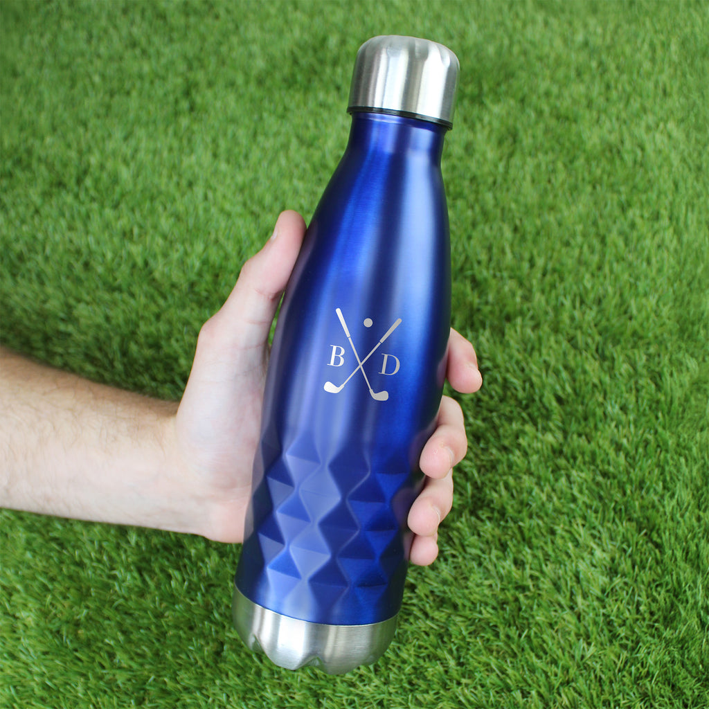 Blue water bottle with silver cap held by a hand on green grass
