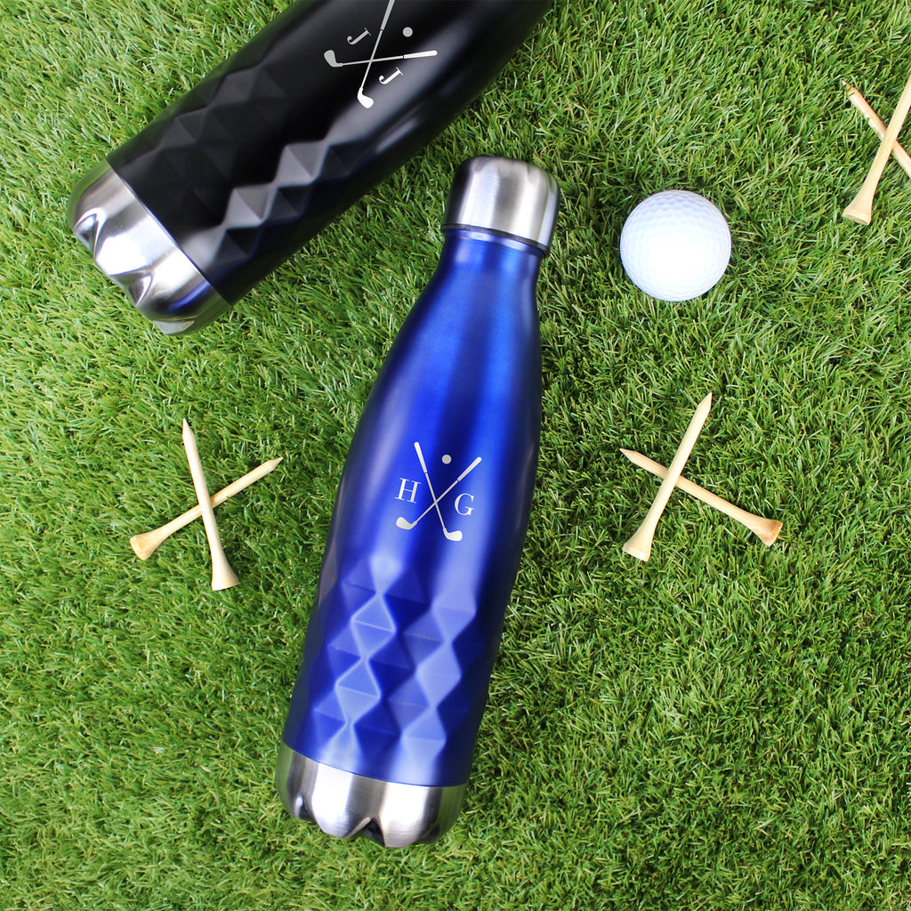 Blue and black water bottles on grass with golf tees and a ball