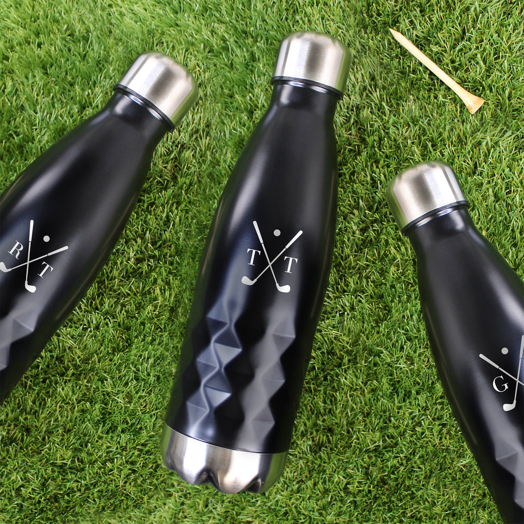 Three black water bottles with silver caps on a grassy surface