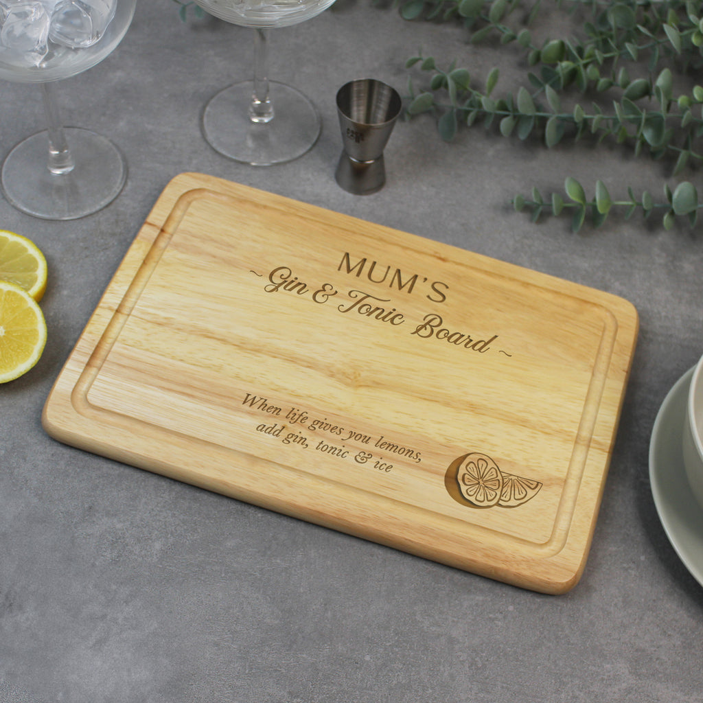 Wooden cutting board with engraved text on a gray surface with drinks and garnishes.
