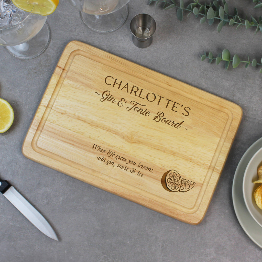 Wooden cutting board with engraved text on a table with drinks and garnishes.