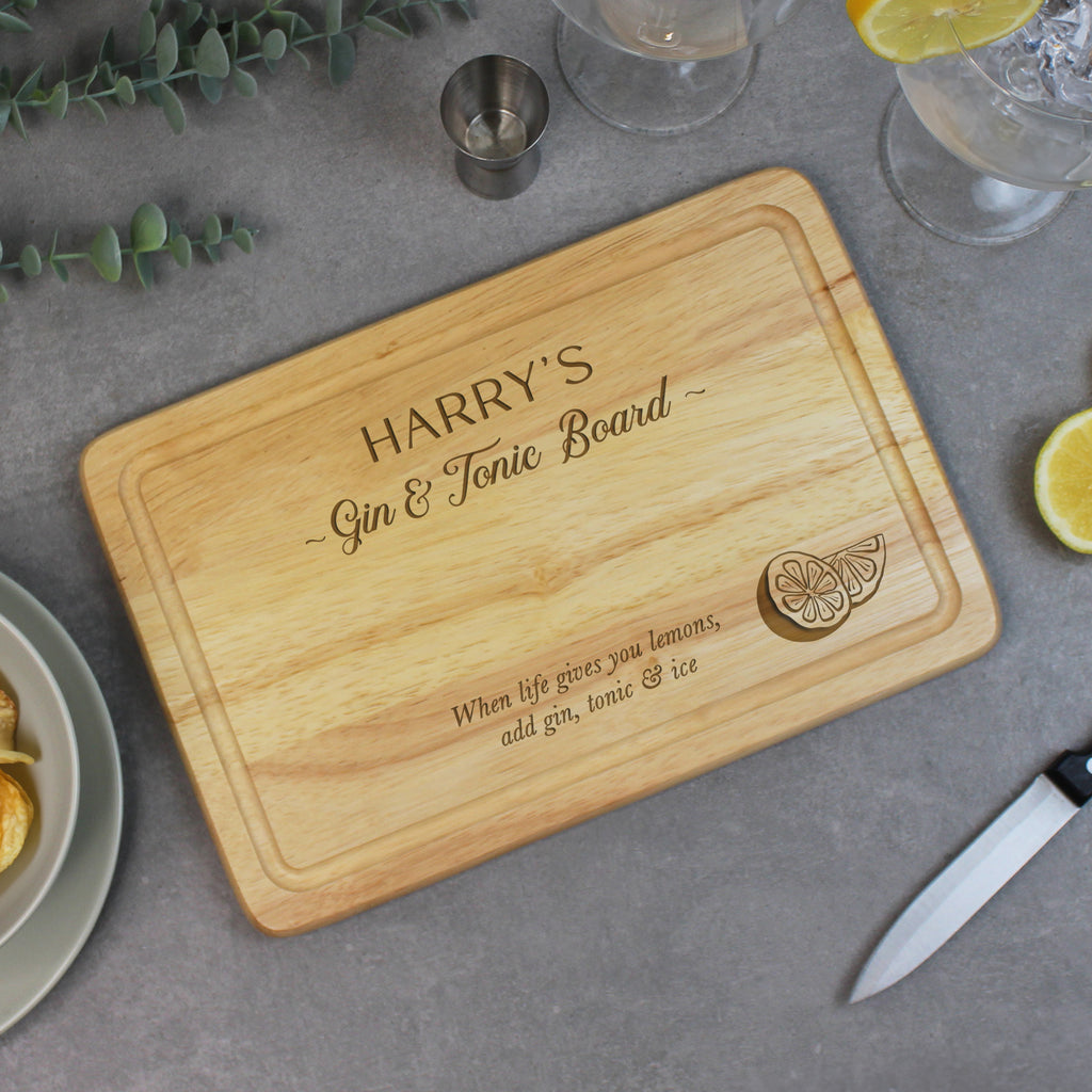 Wooden cutting board with engraved text on a gray surface with drinks and garnishes.