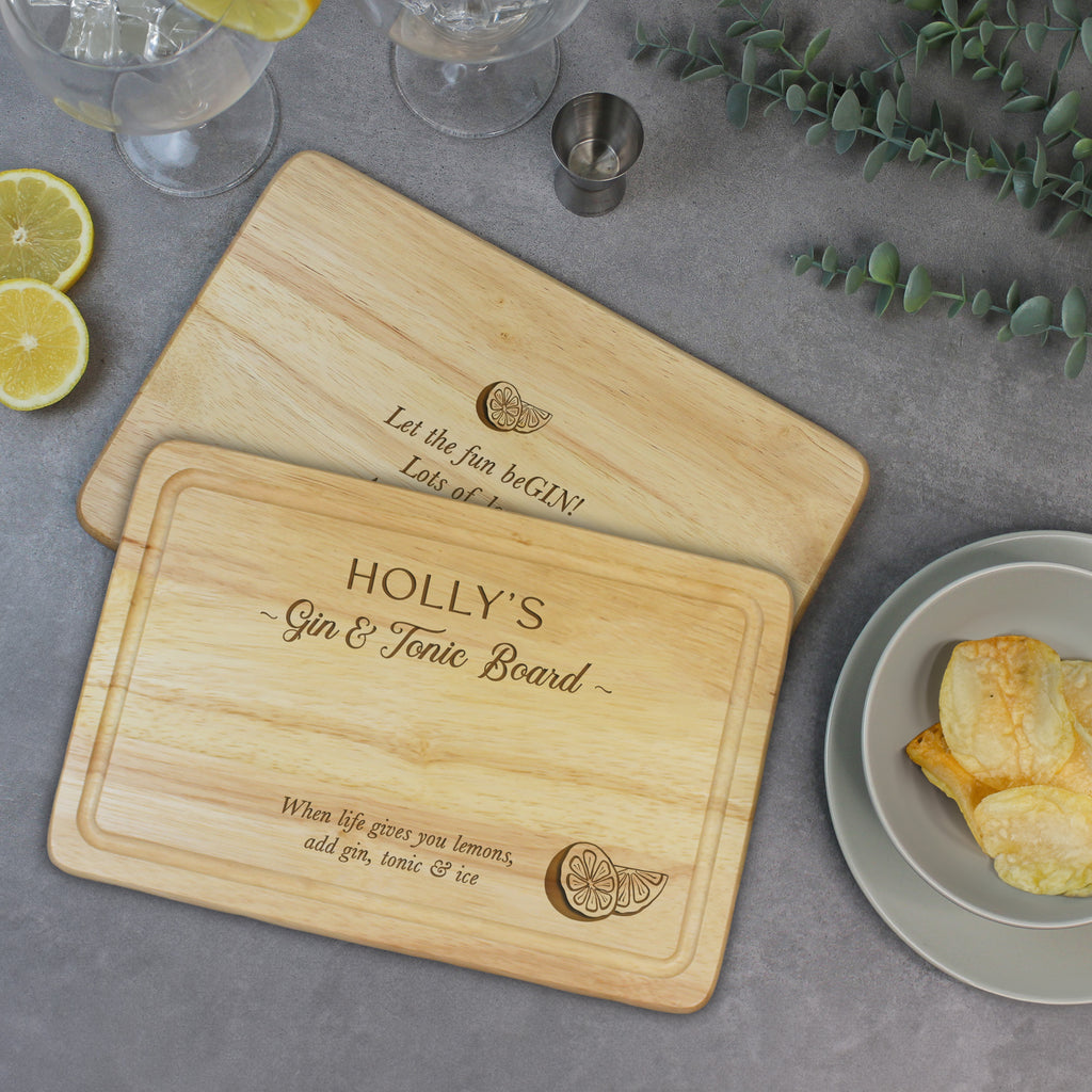Wooden cutting board with engraved text on a table with lemon slices and a plate of snacks.