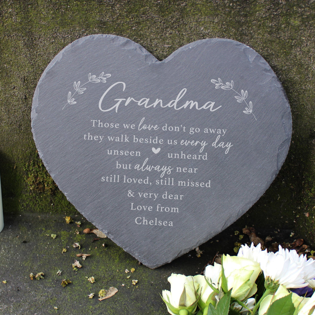 Heart-shaped slate plaque with engraved text on a stone surface with a candle and flowers.