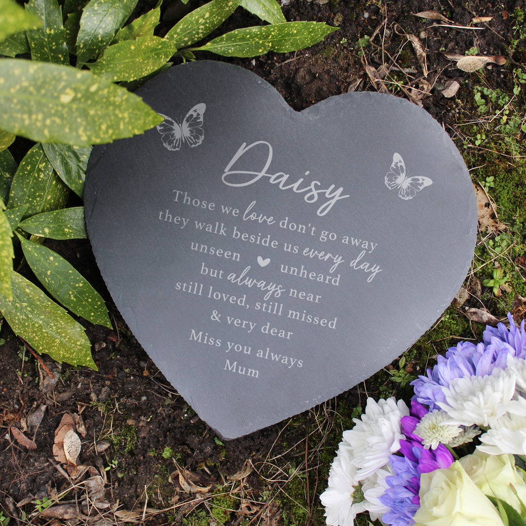 Heart-shaped memorial plaque with engraved text on a garden setting with flowers and leaves.
