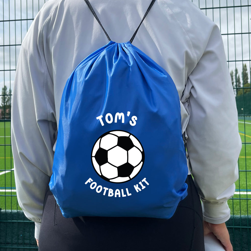 Blue drawstring bag with a soccer ball design and 'Tom's Football Kit' text, worn by a person on a sports field.