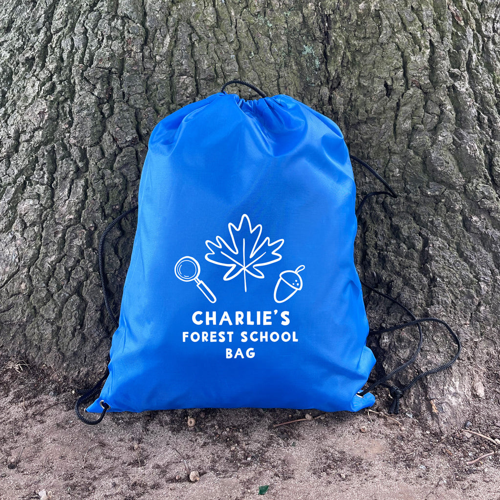 Blue drawstring bag labeled 'Charlie's Forest School Bag' against a tree trunk.