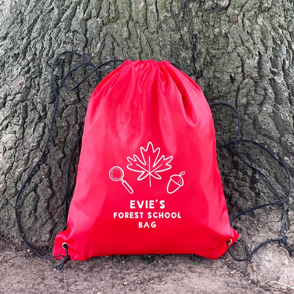 Red drawstring bag with 'Evie's Forest School Bag' text and nature-themed design against a tree trunk.