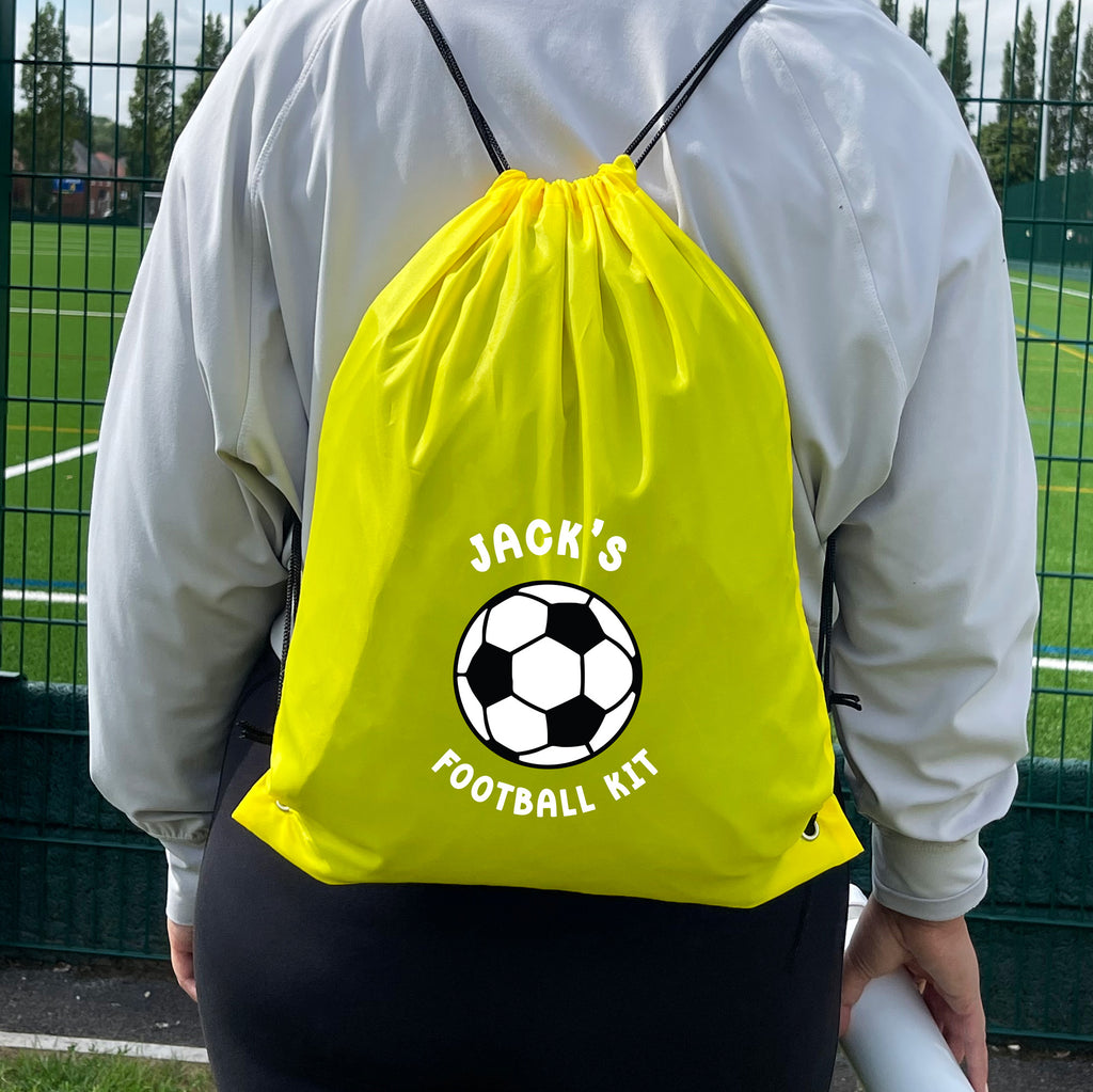 Person wearing a bright yellow drawstring bag with 'Jack's Football Kit' text and soccer ball graphic on a sports field.