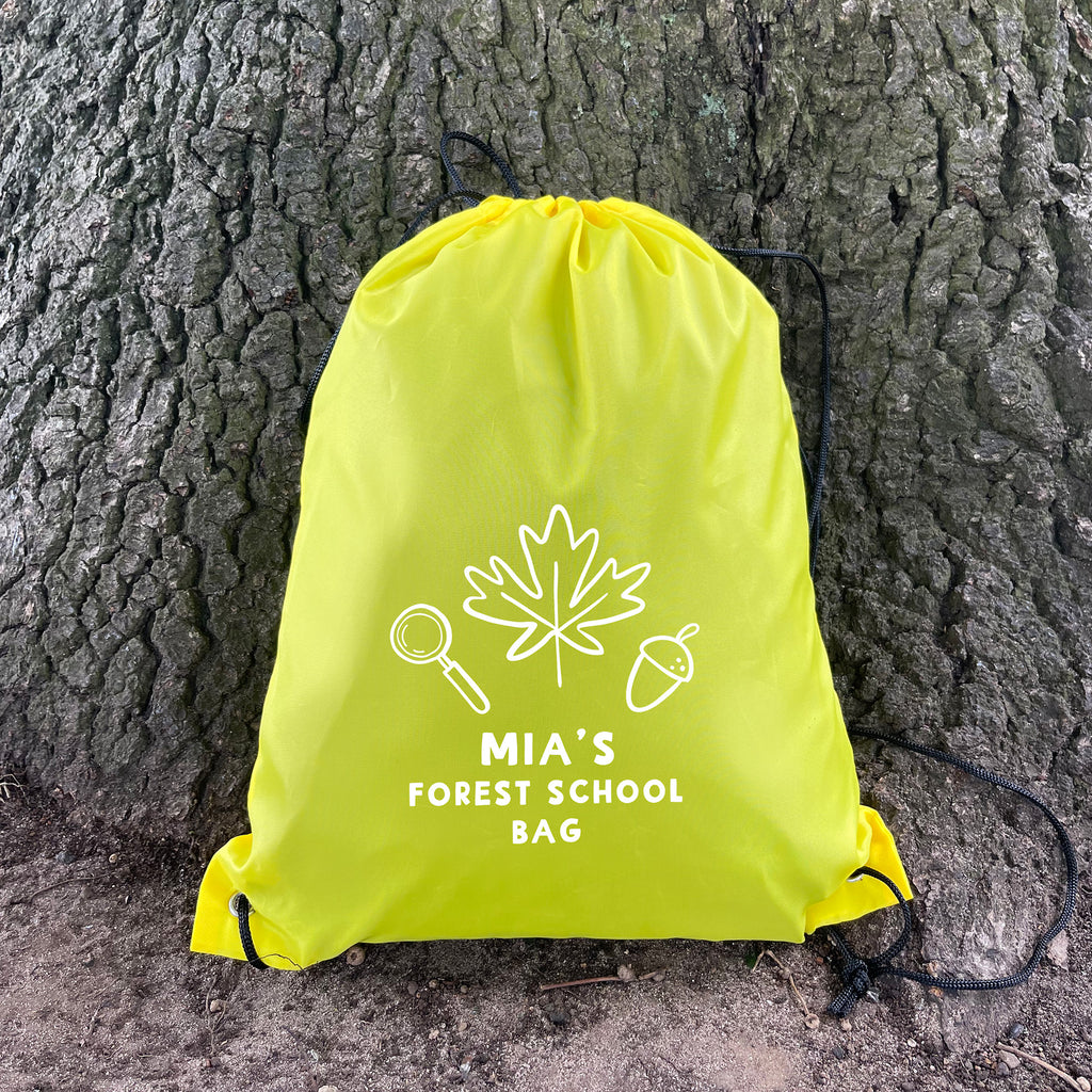 Yellow drawstring bag with 'Mia's Forest School Bag' text and nature-themed design against a tree trunk.