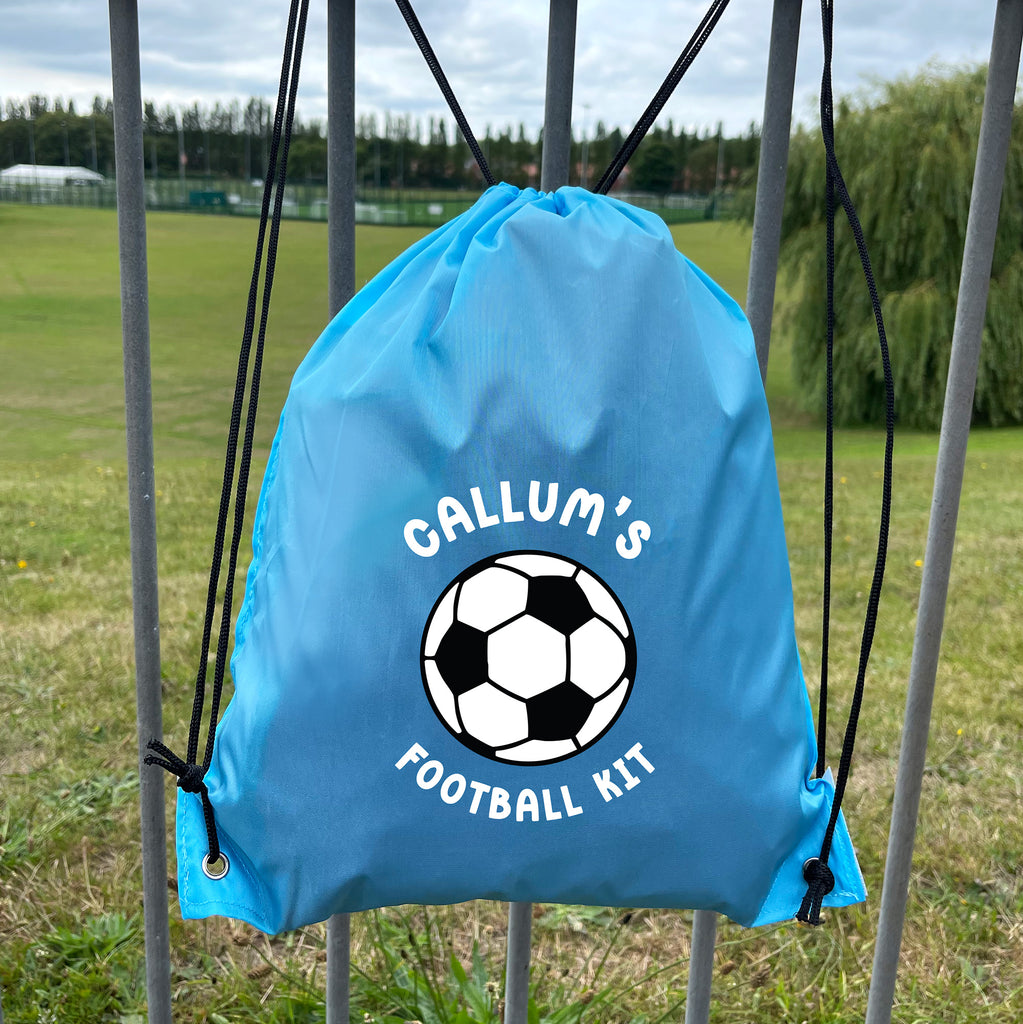 Blue drawstring bag with a soccer ball design and text, placed against a grassy field background.