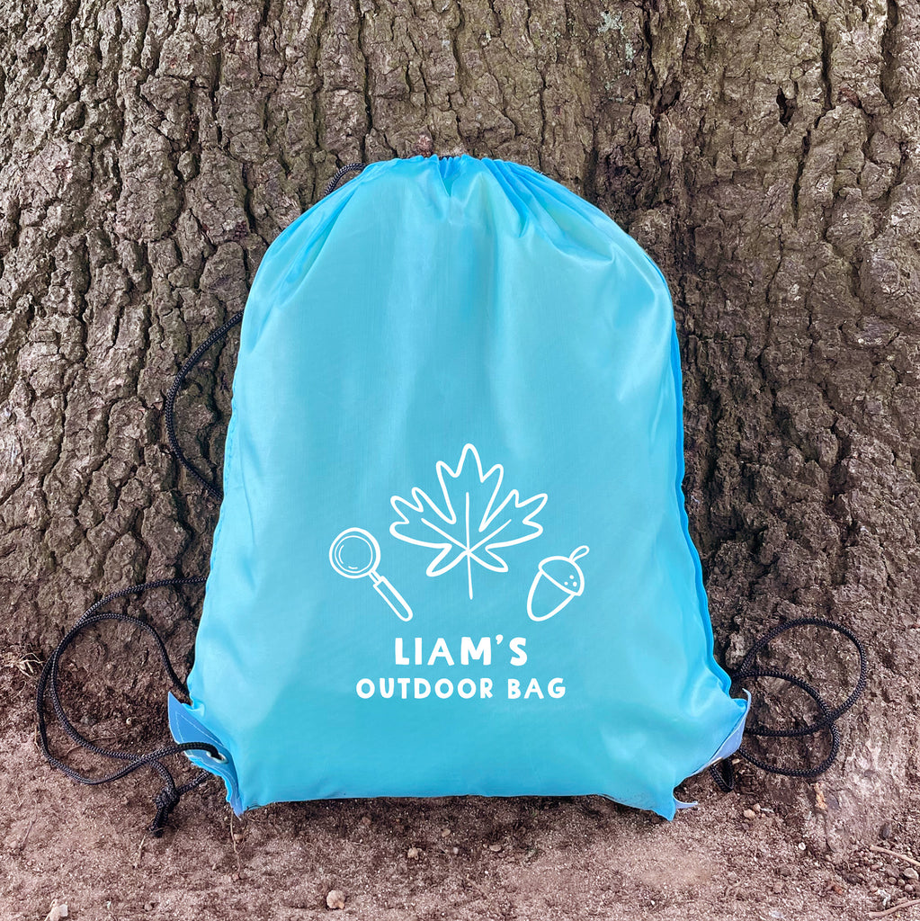 Blue drawstring bag with 'Liam's Outdoor Bag' text and nature-themed design against a tree trunk.