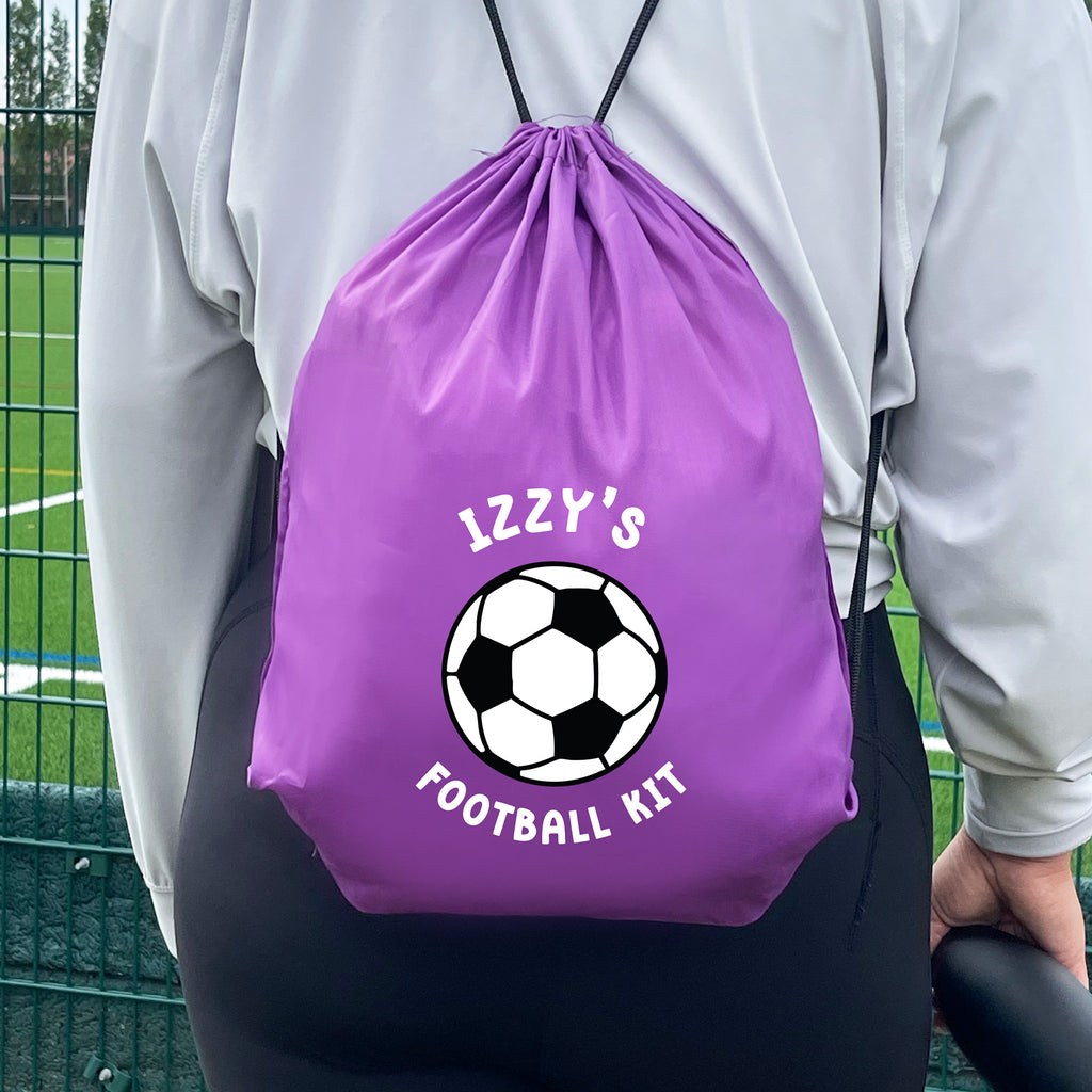 Purple drawstring bag with soccer ball design and 'IZZY'S FOOTBALL KIT' text, worn by a person on a sports field.