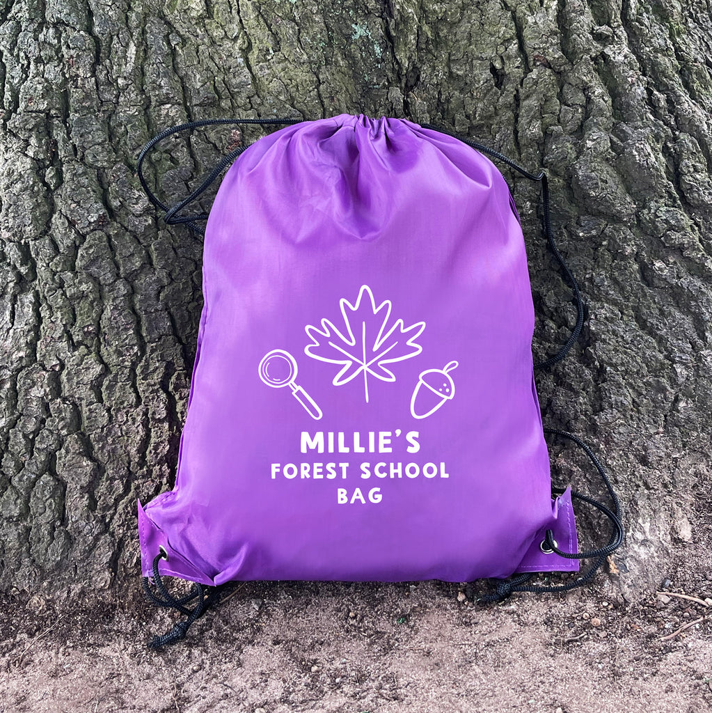 Purple drawstring bag with 'Millie's Forest School Bag' text and leaf design against a tree trunk.