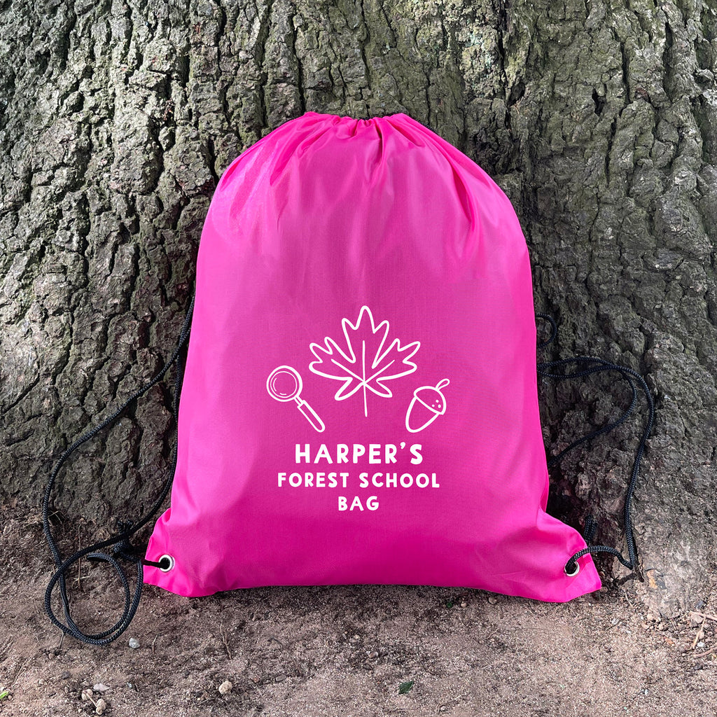 Pink drawstring bag with 'Harper's Forest School Bag' text and design against a tree trunk.