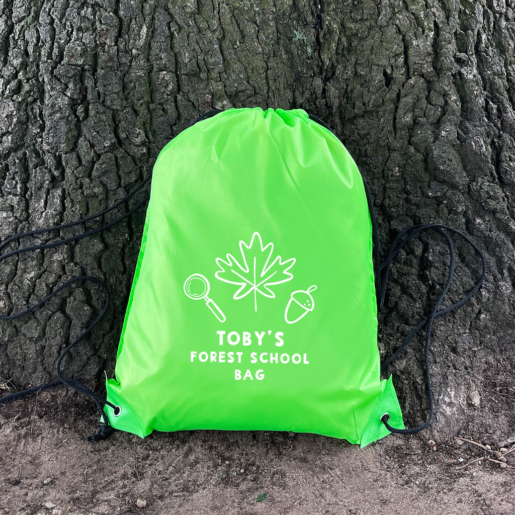 Green drawstring bag with 'Toby's Forest School Bag' text and graphics against a tree trunk.