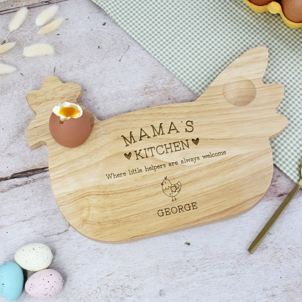 Wooden cutting board shaped like a chicken with 'Mama's Kitchen' engraving on a table with Easter eggs.