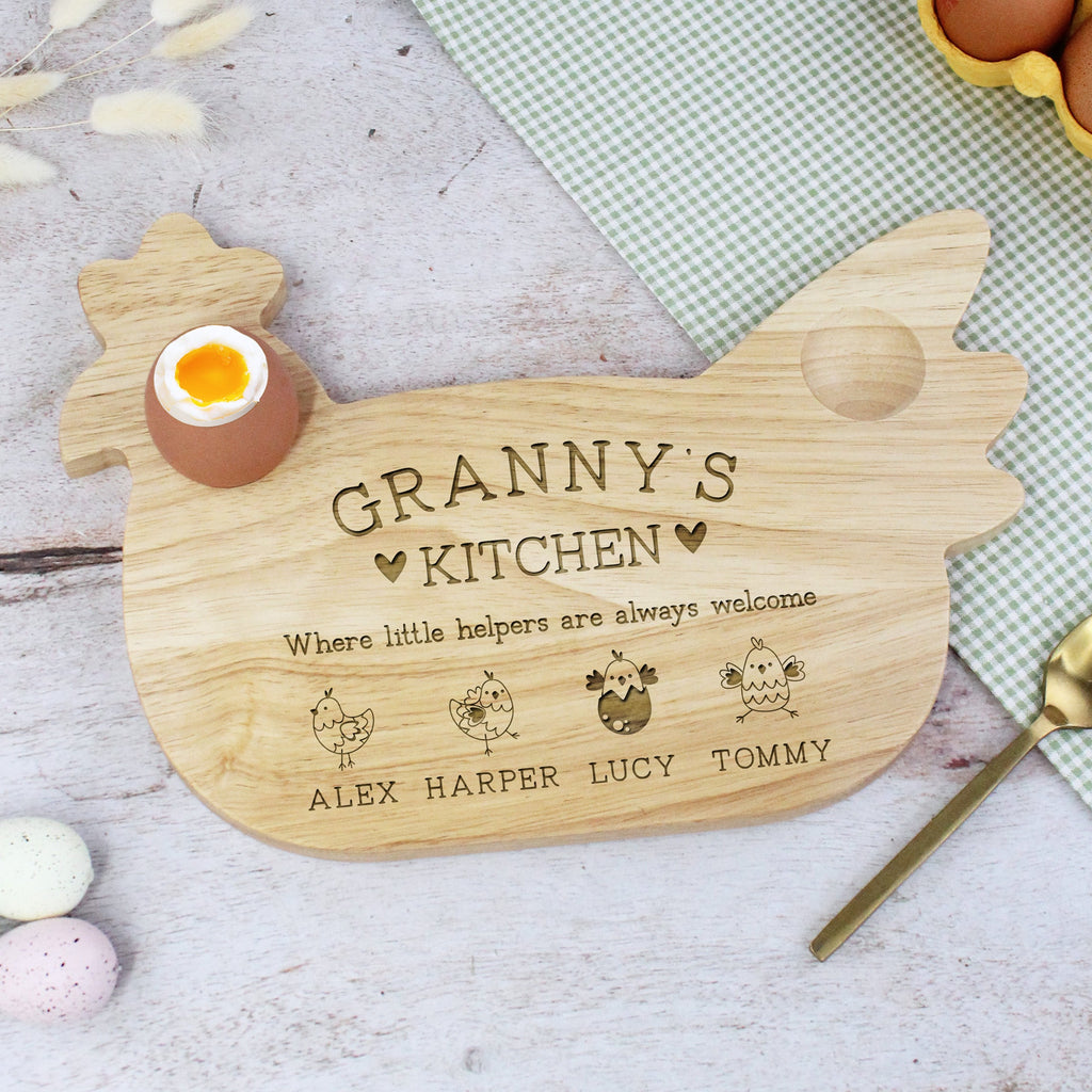 Wooden cutting board shaped like a chicken with engraved text on a table with eggs and a spoon.