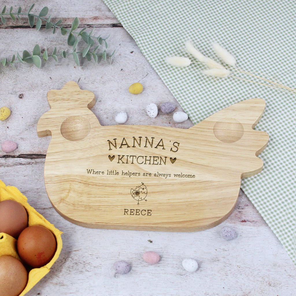 Wooden cutting board shaped like a chicken with engraved text on a wooden surface with eggs and eucalyptus leaves.