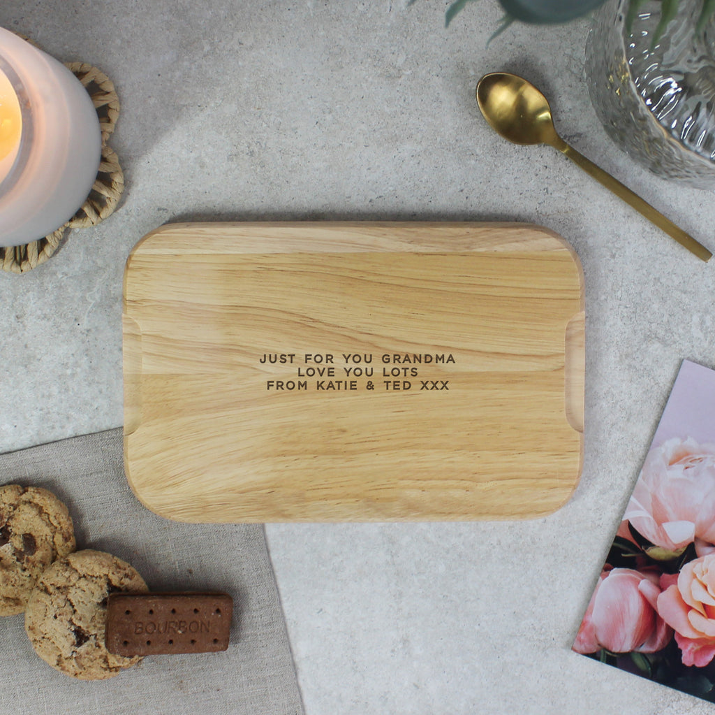 Wooden cutting board with engraved message on a table with cookies and a candle.