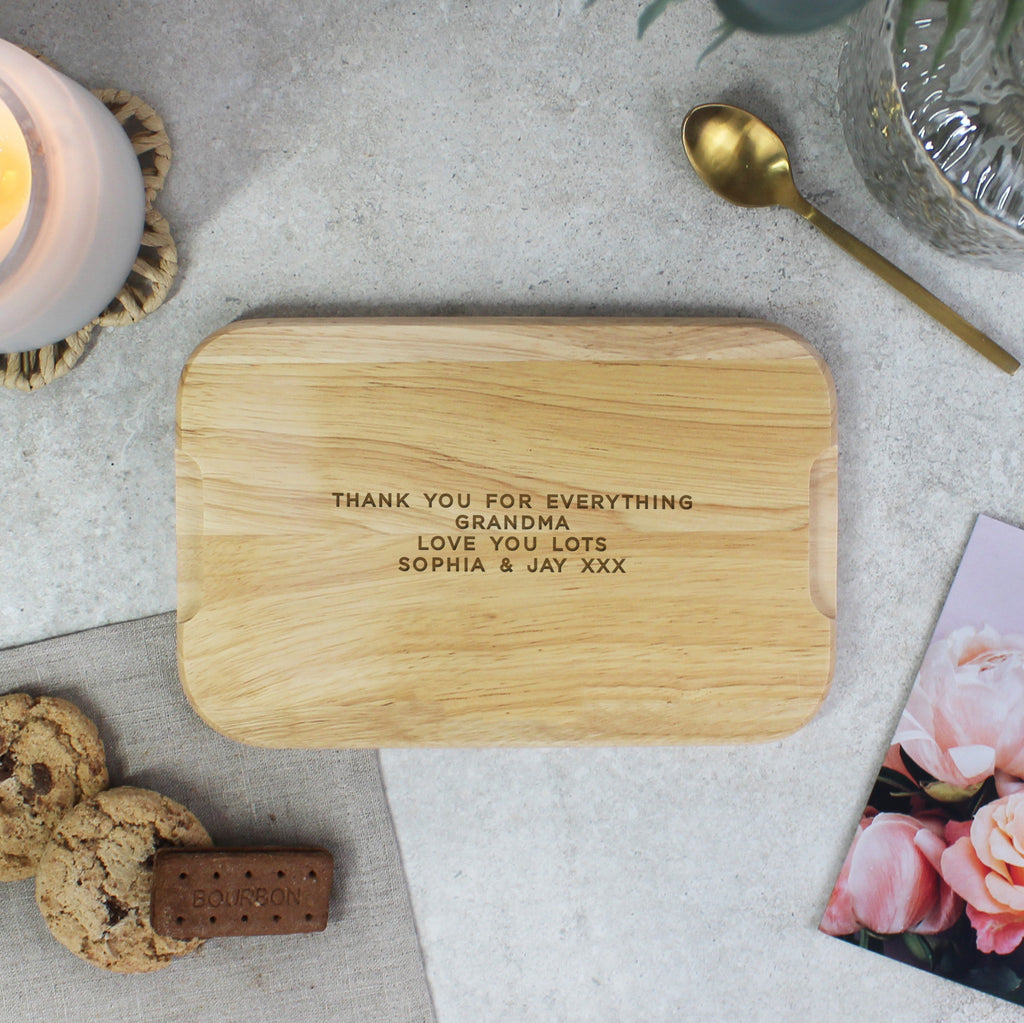 Wooden cutting board with engraved message on a table with cookies and a candle.