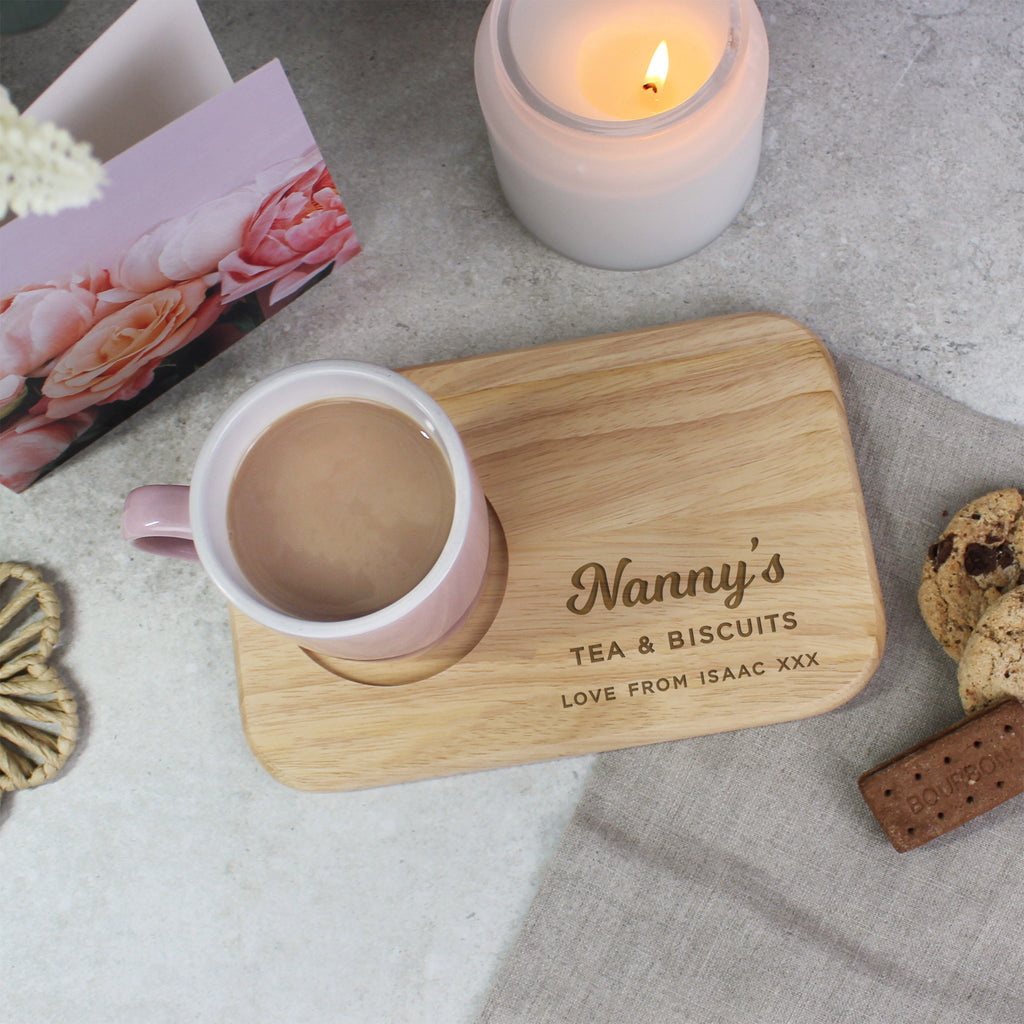 Personalized wooden coaster with 'Nanny's Tea & Biscuits' text, pink mug, and cookies on a light surface.