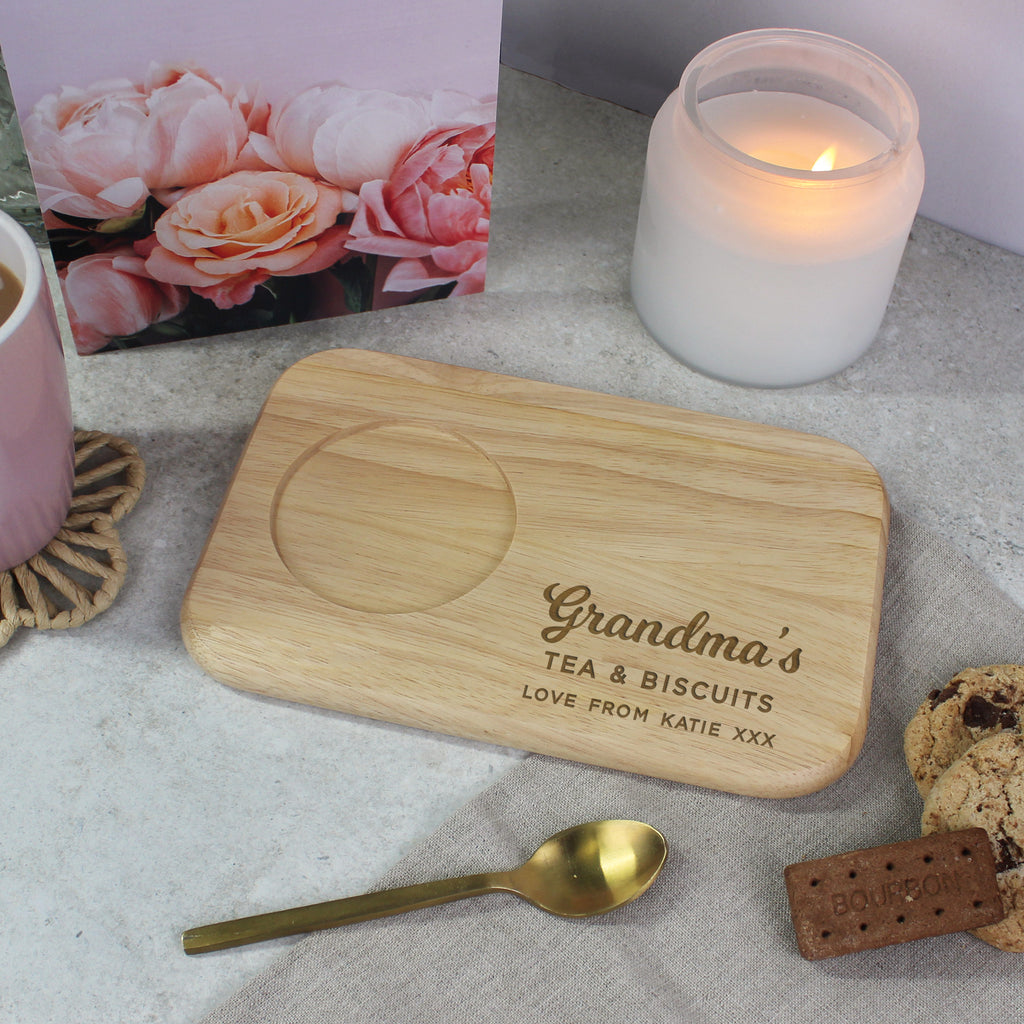 Wooden tray with 'Grandma's Tea & Biscuits' engraving on a table with a candle and cookies.