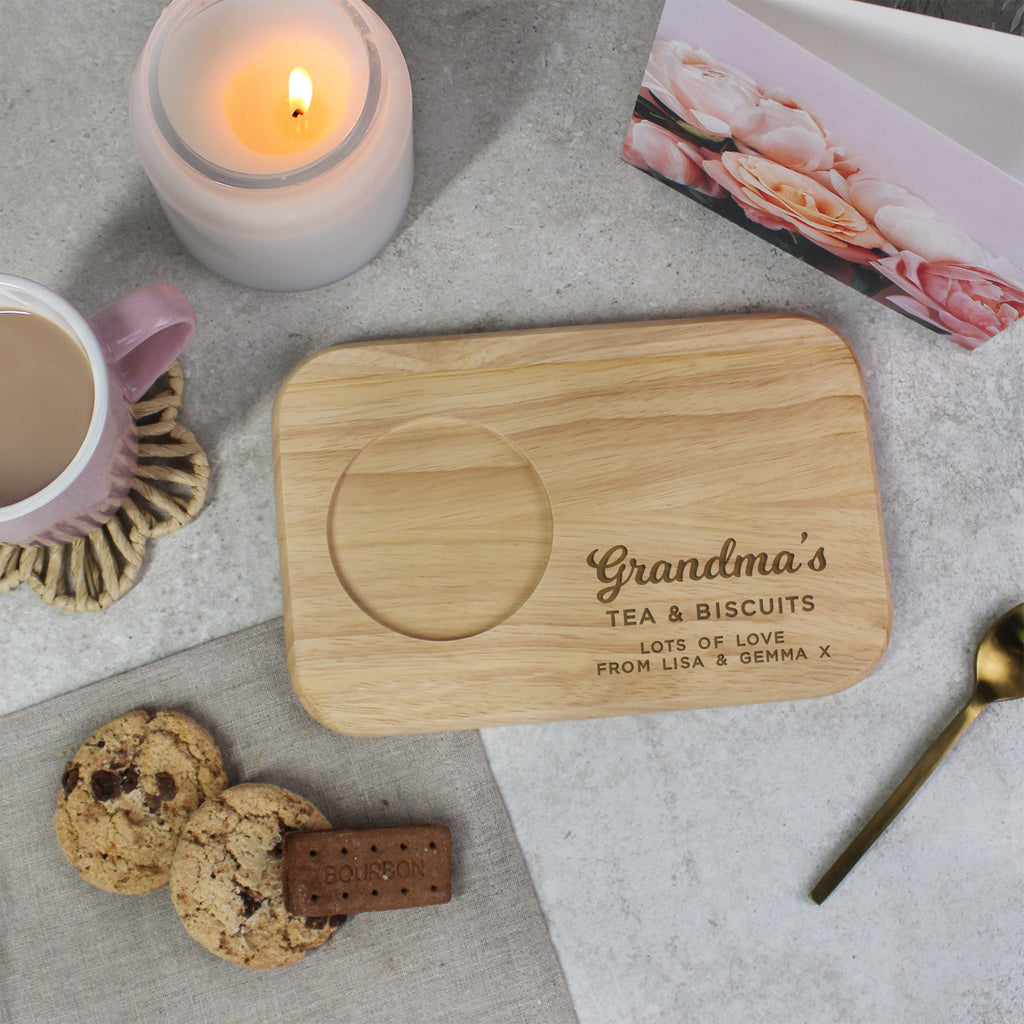 Personalized wooden tray with 'Grandma's Tea & Biscuits' text, cookies, and a candle on a table.