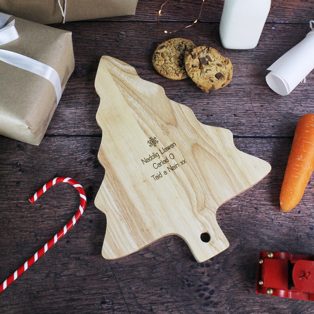 Wooden Christmas tree cutting board with engraved text on a wooden surface with cookies and a carrot.