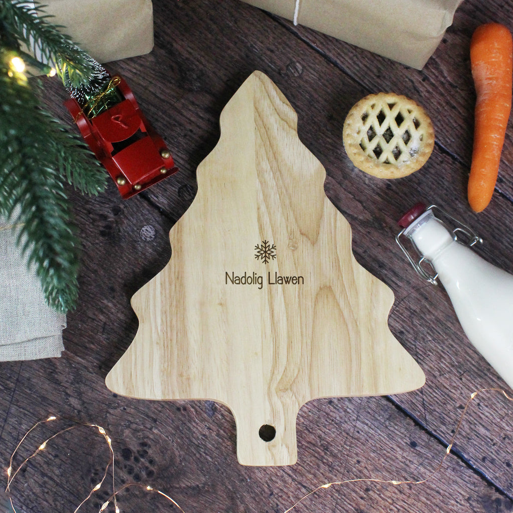 Wooden Christmas tree cutting board with 'Nadolig Llawen' branding on a festive wooden surface.